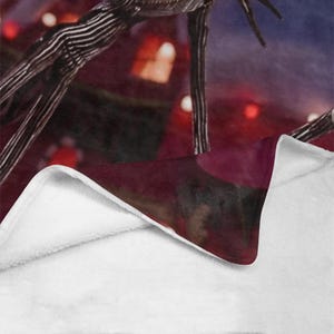 May include: A red and black striped blanket with a white fleece lining. The blanket features a close-up of a character from the movie "The Nightmare Before Christmas".