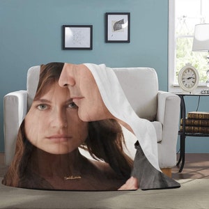 May include: A white throw blanket with a printed image of a couple embracing. The woman is wearing a gold necklace with the word "Self Love" inscribed on it.