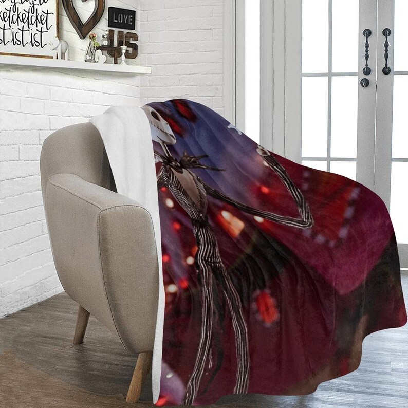 May include: A red and black fleece throw blanket with a white sherpa backing features a printed image of Jack Skellington from the Nightmare Before Christmas movie. The image shows Jack Skellington standing in front of a red and white background with lights.