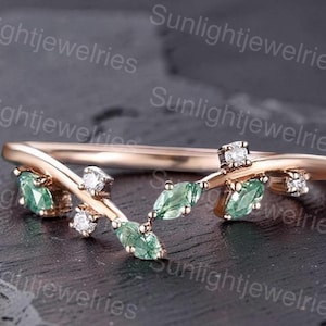 Può includere: Un anello in oro rosa con una fascia a forma di V decorata con pietre verdi taglio marquise e piccole pietre rotonde trasparenti disposte a forma di foglia. La fascia in metallo ha una finitura lucida e le pietre sono incastonate sulla parte superiore.