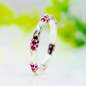 May include: A silver band ring with a twisted design and a row of small, red ruby stones set around the band.