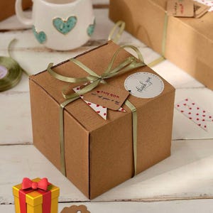 May include: A square brown cardboard gift box tied with a sage green ribbon. A round white sticker reads "thank you for supporting my small business" and a brown paper tag reads "This is made for you with love" with a small red heart icon.