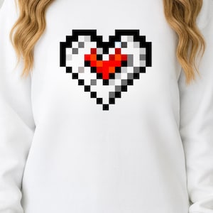 May include: White sweatshirt with a pixelated heart design. The heart is outlined in black with a red centre, and a white and grey fill. The sweatshirt is a casual style, suitable for everyday wear.