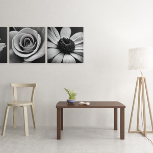 May include: A white chair with a wooden frame sits next to a brown coffee table with a small potted plant on top. A white lamp with a wooden tripod base stands in the corner of the room. Three black and white flower photographs hang on the wall.