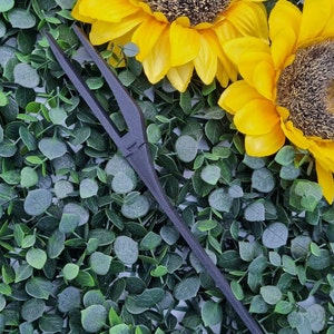 Può includere: Un pettine per capelli nero con un manico lungo e sottile. Il pettine è appoggiato su un letto di fogliame artificiale verde.