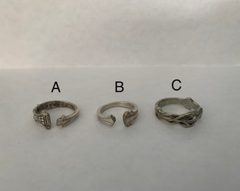 May include: Three silver rings with different designs. The ring labelled A has a detailed design with a gap in the band. The ring labelled B has a simple design with a gap in the band. The ring labelled C has a braided design.