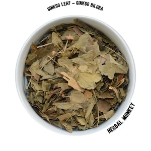 Könnte beinhalten: Eine weiße Schüssel gefüllt mit getrockneten Ginkgoblättern. Die Schüssel ist mit "GINKGO LEAF - GINKGO BILOBA" und "HERBAL MONKEY" beschriftet.