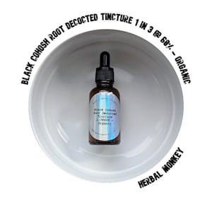 Op de afbeelding: Een bruine glazen fles met een zwarte druppelaar, met het label "Black Cohosh Root Decocted Tincture". De fles staat in een witte kom, met tekst rond de kom met de tekst "Herbal Monkey" en "Organic".