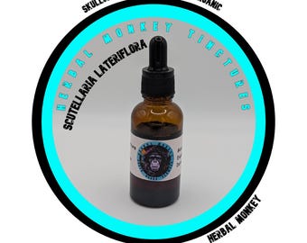 May include: A brown glass bottle with a black dropper top, containing a dark liquid. The bottle has a label with a monkey graphic and text. The bottle is centered within a circular design with the text "HERBAL MONKEY TINCTURES" and "SKULLCAP TINCTURE 1:2 @ 35% ORGANIC".