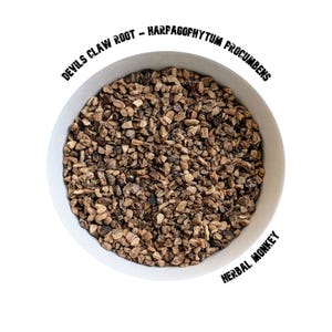 Op de afbeelding: Een witte kom gevuld met kleine, onregelmatig gevormde stukjes Duivelsklauw-wortel (Harpagophytum procumbens). De tekst "DEVILS CLAW ROOT - HARPAGOPHYTUM PROCUMBENS" staat boven de kom en "HERBAL MONKEY" is eronder gedrukt.