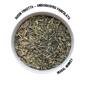 Op de afbeelding: Een witte kom gevuld met gedroogde groene chiretta, ook bekend als Andrographis paniculata, een soort kruid. De kom is gelabeld met "GREEN CHIRETTA - ANDROGRAPHIS PANICULATA" en "HERBAL MONKEY".