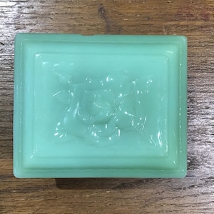 Puede incluir: Una caja de vidrio verde vintage para guardar pequeños objetos con un diseño floral en relieve en la tapa.