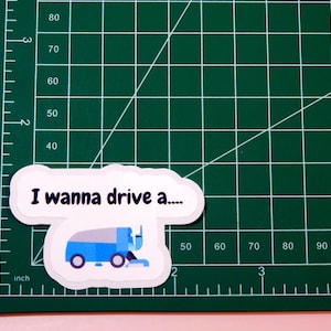 May include: A white sticker with a blue and white cartoon image of a street sweeper and the text "I wanna drive a..."
