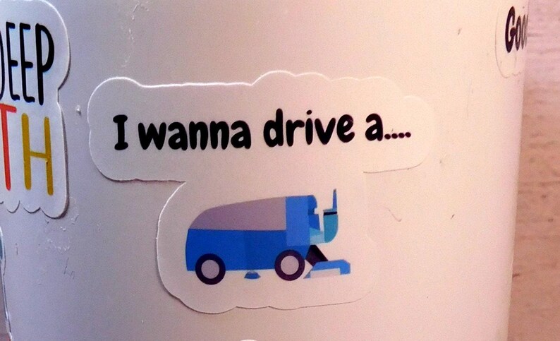 May include: A white sticker with the text "I wanna drive a..." and a blue and gray cartoon illustration of a snowplow.