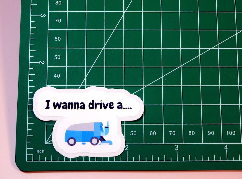 May include: A white sticker with a blue and gray cartoon illustration of a snow plow truck. The sticker says "I wanna drive a..."