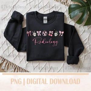 Puede incluir: Sudadera negra con texto 'Radiology' en rosa e iconos decorativos. El diseño incluye lazos, un signo de la paz, un símbolo de radiación, cerezas y manos de esqueleto. Mangas con puños.
