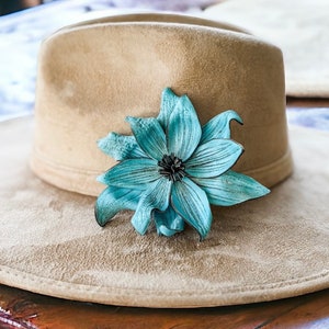 May include: A light brown suede hat with a wide brim and a teal blue leather flower accent.