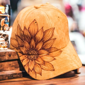 May include: A brown suede baseball cap with a brown sunflower design on the side.