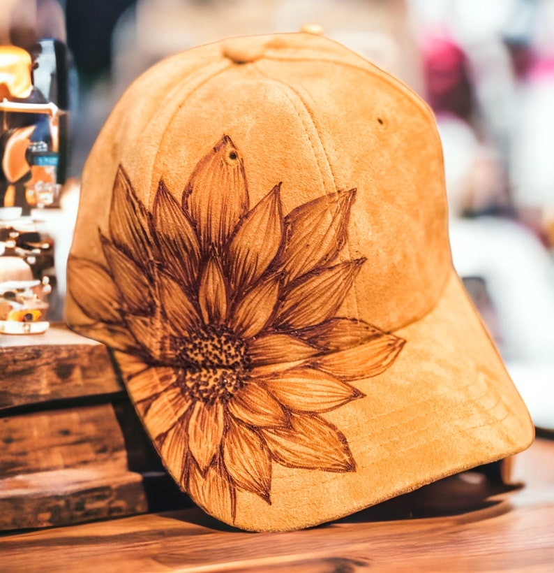 May include: A brown suede baseball cap with a brown sunflower design on the side.