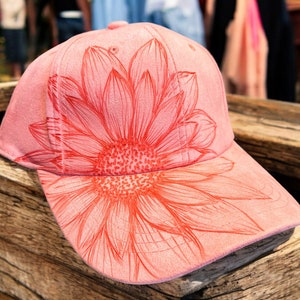 May include: A pink suede baseball cap with a red sunflower design.
