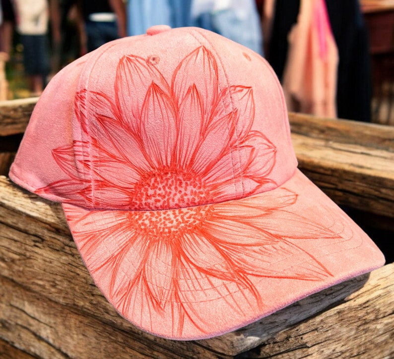 May include: A pink suede baseball cap with a red sunflower design.