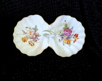 May include: A white porcelain double dish with a gold rim and floral design. The dish is shaped like two scallop shells joined together by a handle.