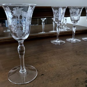May include: Set of six clear glass wine glasses with etched floral designs. The glasses have a tall, slender stem and a wide, round bowl.