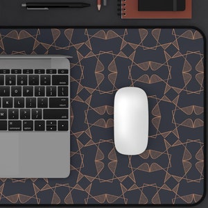 May include: A black laptop computer with a silver keyboard and trackpad is on a dark blue desk mat with a geometric pattern. A white wireless mouse is on the desk mat. A small potted plant, a cup of coffee, a pen, and two pencils are also on the desk.