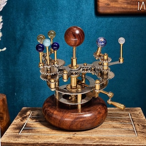 Può includere: Un modello meccanico di orrery con una grande sfera centrale in legno che rappresenta il sole, circondata da sfere più piccole di vari colori e materiali montate su ingranaggi e bracci in ottone, su una base circolare in legno.