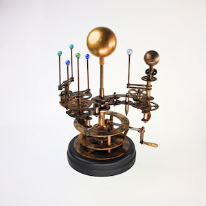 May include: A brass and gold-toned model of the solar system with a hand crank. The model features a central sun with planets orbiting around it. The planets are represented by small glass spheres in various colors.