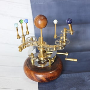 May include: A wooden base with a brass and silver gear system that rotates a wooden sphere representing the sun and smaller glass spheres representing the planets.