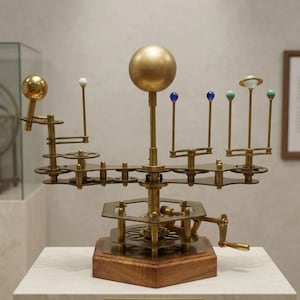 May include: A brass and wood model of the solar system, featuring a large golden sphere representing the sun, with smaller spheres and gears representing the planets. The model is mounted on a wooden base and includes a hand crank.