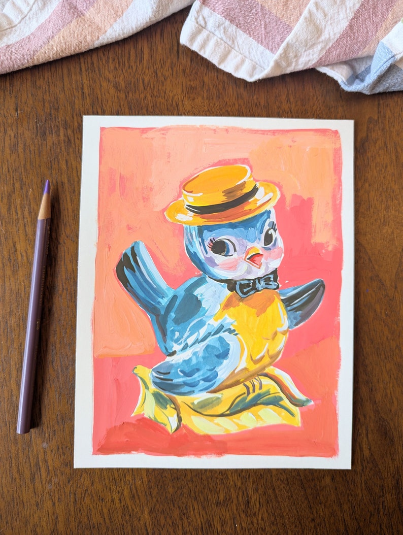 Op de afbeelding: Een handgeschilderde illustratie van een blauwe vogel die een gele hoed en een zwarte strik draagt. De vogel zit op een geel blad met een roze achtergrond.