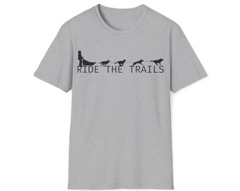 Puede incluir: Una camiseta gris jaspeado con un gráfico negro de una persona tirada por perros. El texto "RIDE THE TRAILS" está impreso debajo del gráfico en una fuente sans-serif.