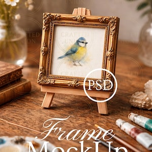 Puede incluir: Una pequeña pintura enmarcada en oro de un pájaro azul y amarillo sobre un caballete de madera. El marco tiene detalles ornamentados. Las palabras "Frame MockUp" se muestran debajo. Se ven tubos de pintura y pinceles.