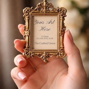 Puede incluir: Un pequeño marco dorado y ornamentado sostenido en una mano. El marco tiene detalles intrincados y el texto "Your Art Here" es visible. Las dimensiones del marco son 5x7.6, 10.1x15.2, 20.3x30.4, y 30.4x45.7 cm. The Crafted Union también está impreso.