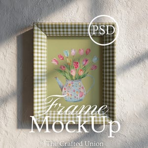 Pode incluir: Uma impressão artística emoldurada com uma ilustração em aquarela de tulipas coloridas em uma chaleira floral. A moldura tem um padrão xadrez verde e branco. O texto "Frame MockUp" e "The Crafted Union" são visíveis.