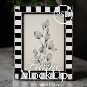 May include: A rectangular picture frame with a black and white striped border. The frame holds a drawing of delicate, linear botanical elements in black and white. The words "Frame MockUp" are displayed in white text.