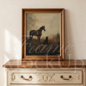 May include: A rectangular framed painting featuring a dark brown horse and a small black dog standing in a misty, grassy field. The artwork is enclosed in a simple wooden frame with a gold inner border, resting on a light-colored wooden dresser.