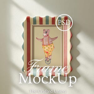 May include: A framed artwork featuring a circus bear riding a unicycle, wearing yellow polka-dot pants and suspenders. The frame has a scalloped edge with red, cream, and blue stripes. The text "Frame MockUp" is displayed at the bottom of the frame.
