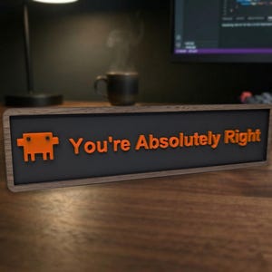 Puede incluir: Un letrero rectangular de madera con el texto "You're Absolutely Right" en letras naranjas. El letrero también presenta un gráfico pixelado naranja. El letrero está sobre un escritorio de madera.
