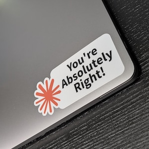 以下が含まれることがあります： 「You're Absolutely Right!」の黒い文字が入った白いステッカー。赤とオレンジの花柄のデザインが施されています。ステッカーはグレーのノートパソコンに貼られており、濃い木目の表面に配置されています。
