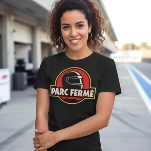 May include: Black t-shirt with a red and yellow graphic featuring a racing helmet and the words "PARC FERMÉ". The design is set within a circular frame. The shirt is made of a soft material.