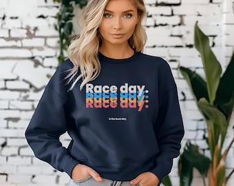 Puede incluir: Una sudadera azul marino con el texto "Race day: Race day: Race day: is the best day" impreso en una fuente colorida y superpuesta.