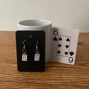 May include: A pair of silver earrings with a small playing card charm. The card is a six of spades.
