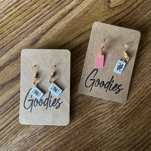 May include: Two pairs of earrings on brown card stock with the word "Goodies" printed on each card. One pair features a red card and the other pair features a Jack of Spades.