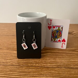 May include: A pair of dangle earrings with a black card design featuring the Queen of Hearts. The earrings are on a black card display.