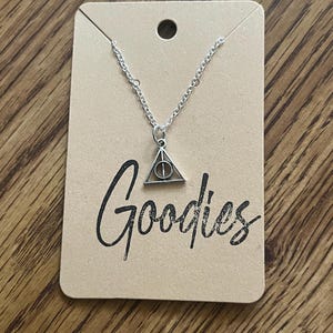 May include: A silver necklace with a silver triangle pendant featuring a circle inside. The pendant is on a brown card with the word "Goodies" written in black.