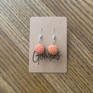 May include: A pair of orange and white dangle earrings with a white polka dot pattern. The earrings are on a brown card with the word "Googles" written on it.