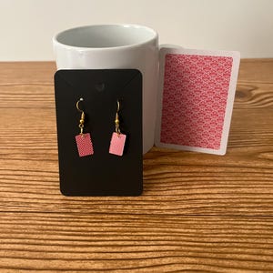 May include: A pair of red playing card earrings on a black display card. The earrings are shaped like a playing card and have a gold hook.